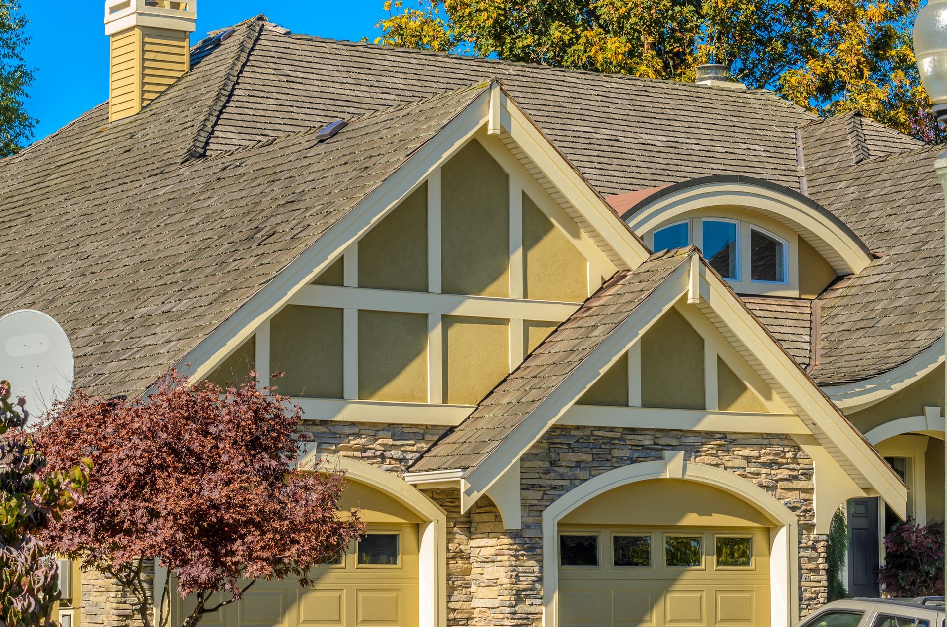 Stone-and-wood suburban house with steep gabled roof, arched windows, and autumn trees in front