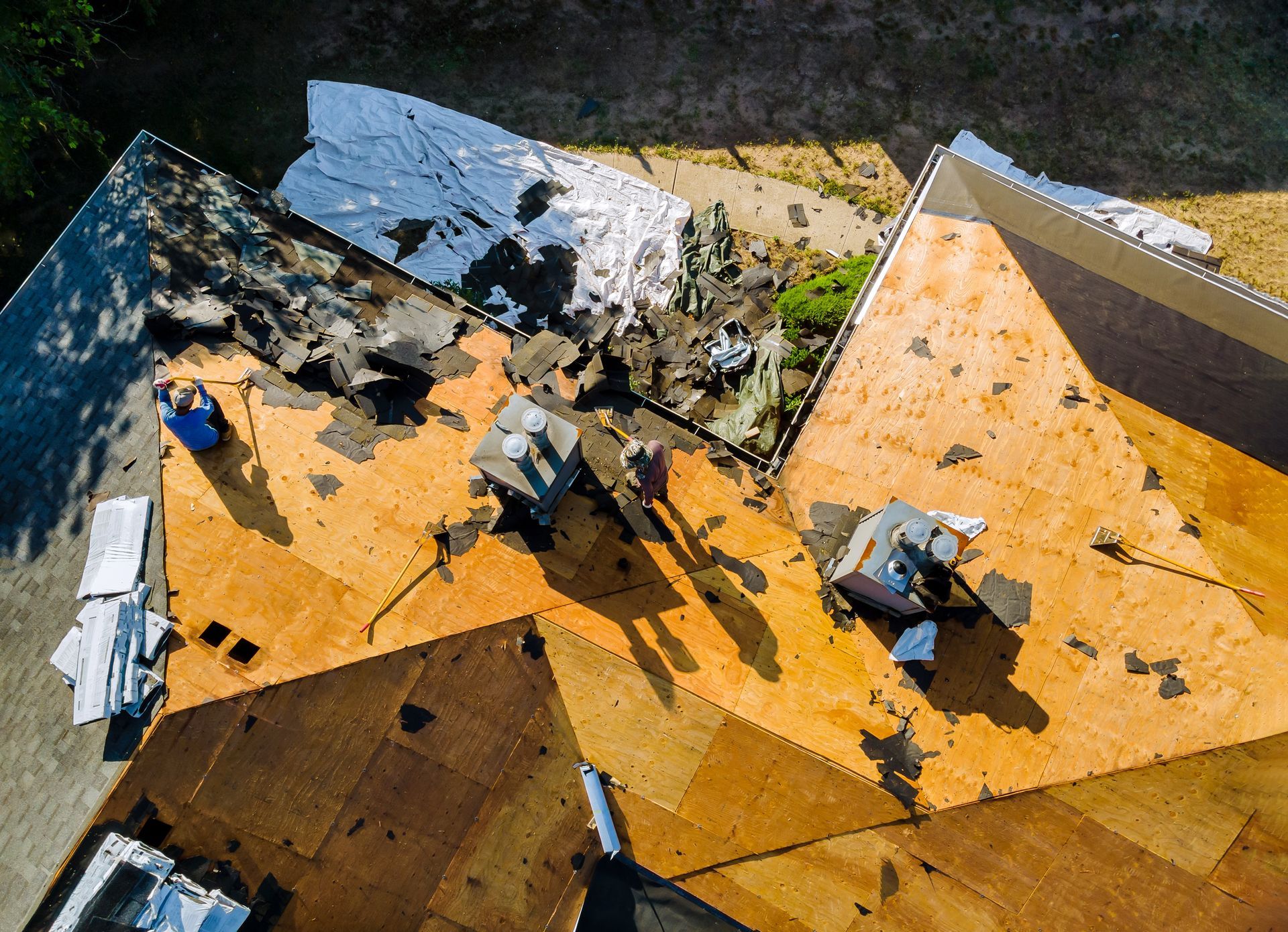 Aerial view of workers on a yellow and white rooftop under construction, with scattered materials and debris.