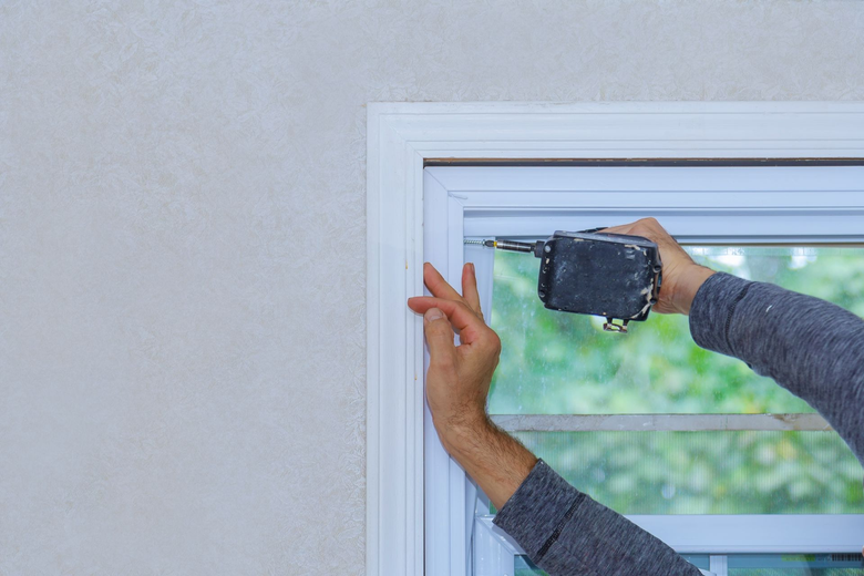 Person using a power drill to install trim around a window.