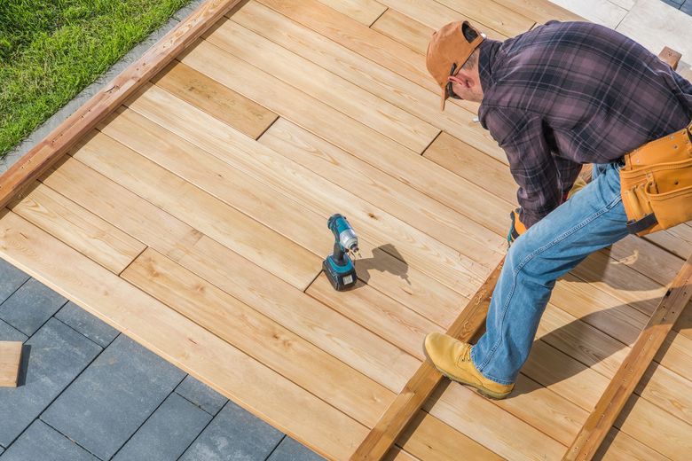 Carpenter installing wooden deck, using a power drill.