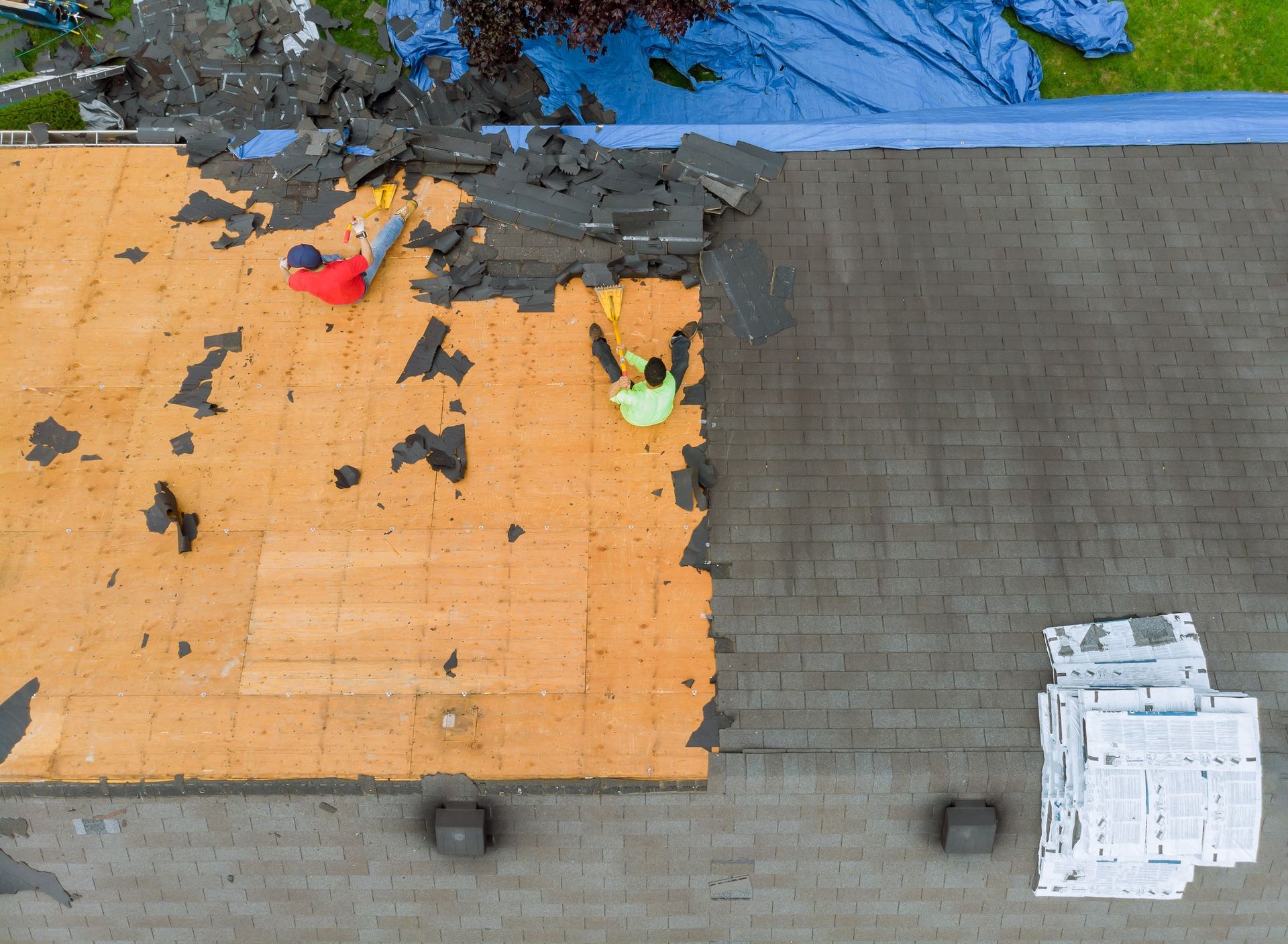 Two workers removing shingles from a roof. Orange underlayment exposed.