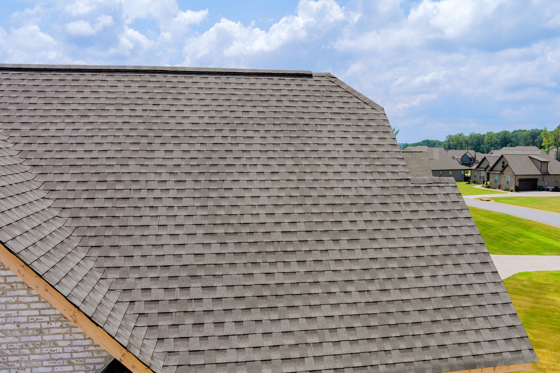 Gray shingled roof in a suburban neighborhood under a partly cloudy sky