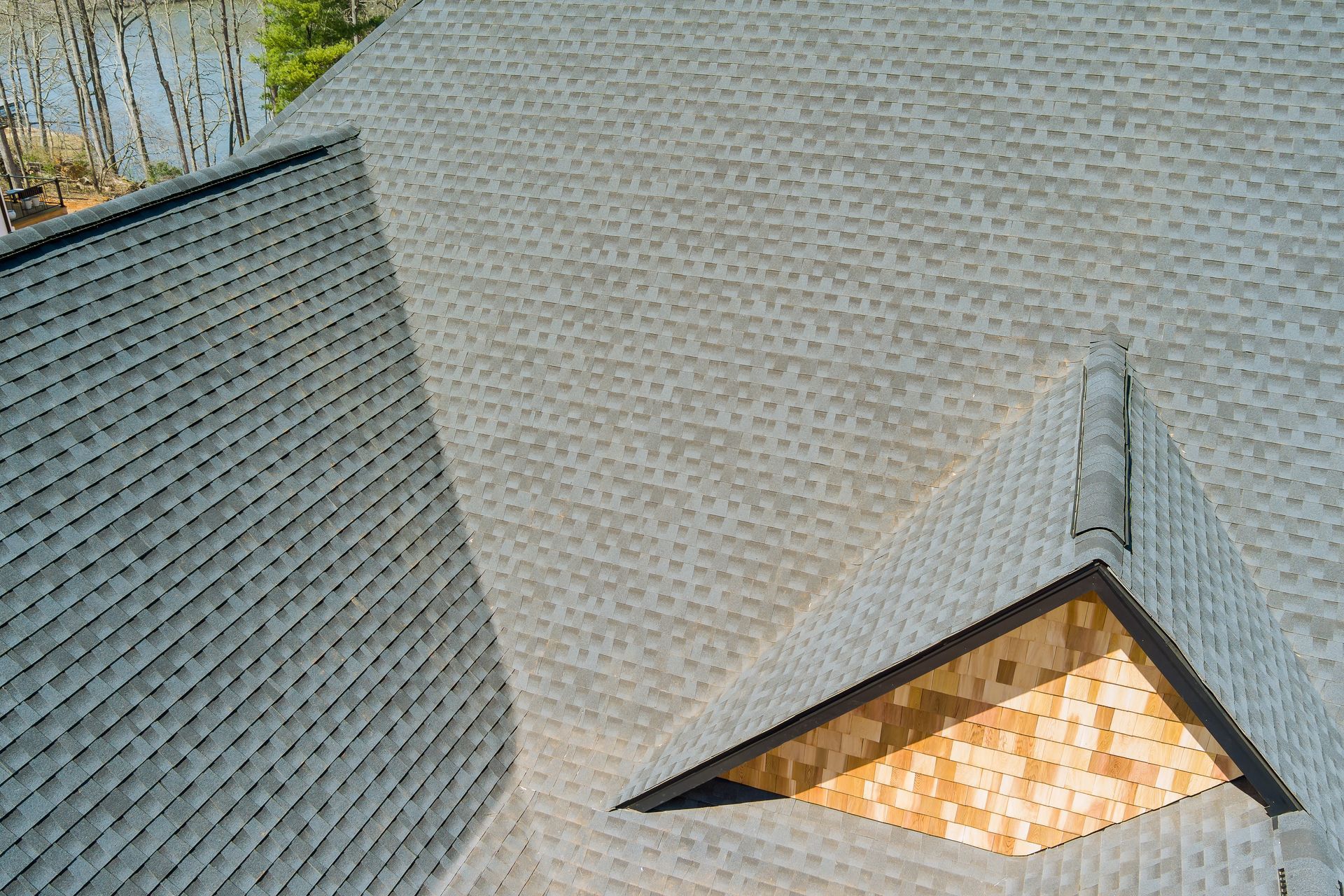 Architectural rooftop with gray shingles and a small triangular dormer window glowing warm light