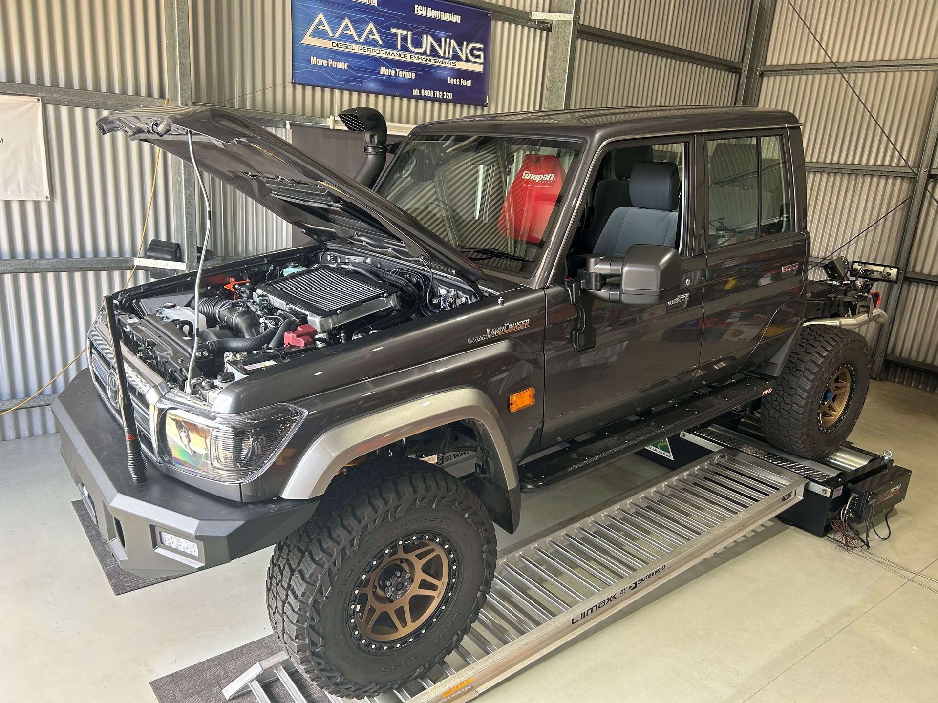 A black Landcruiser 79 series with the hood up is sitting on a ramp in a garage having just had diesel tuning done.