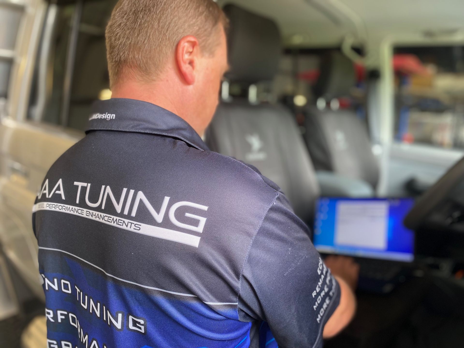 A man wearing a shirt that says aa tuning is working on a car.