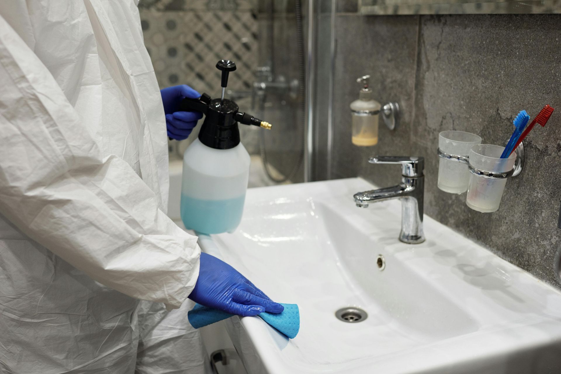 A person in a protective suit is cleaning a bathroom sink.