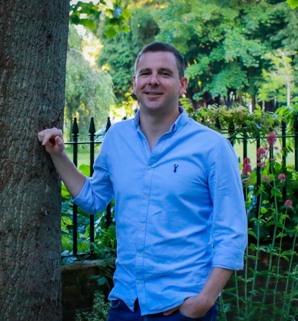 a man in a blue shirt is leaning against a tree in a park .