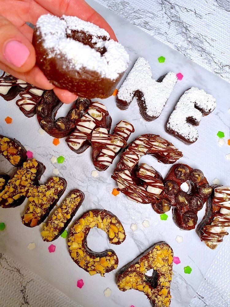 A person is holding a chocolate donut with powdered sugar on top