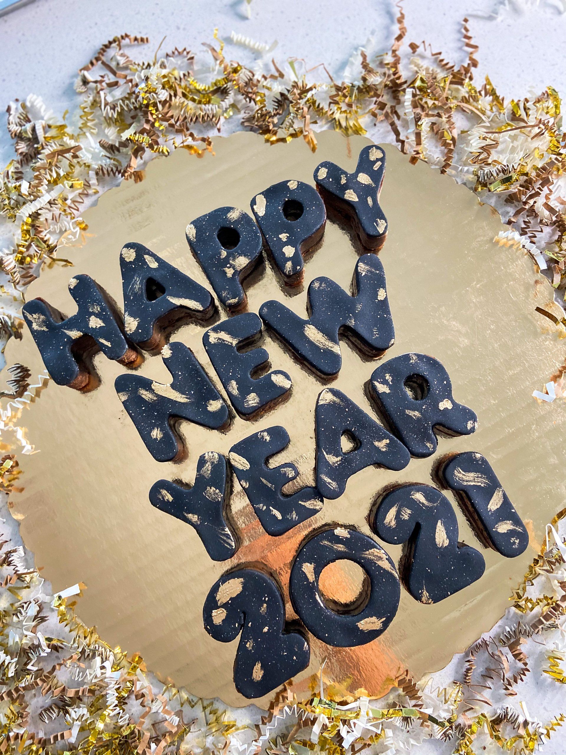 A gold plate topped with black letters that say happy new year 2021.