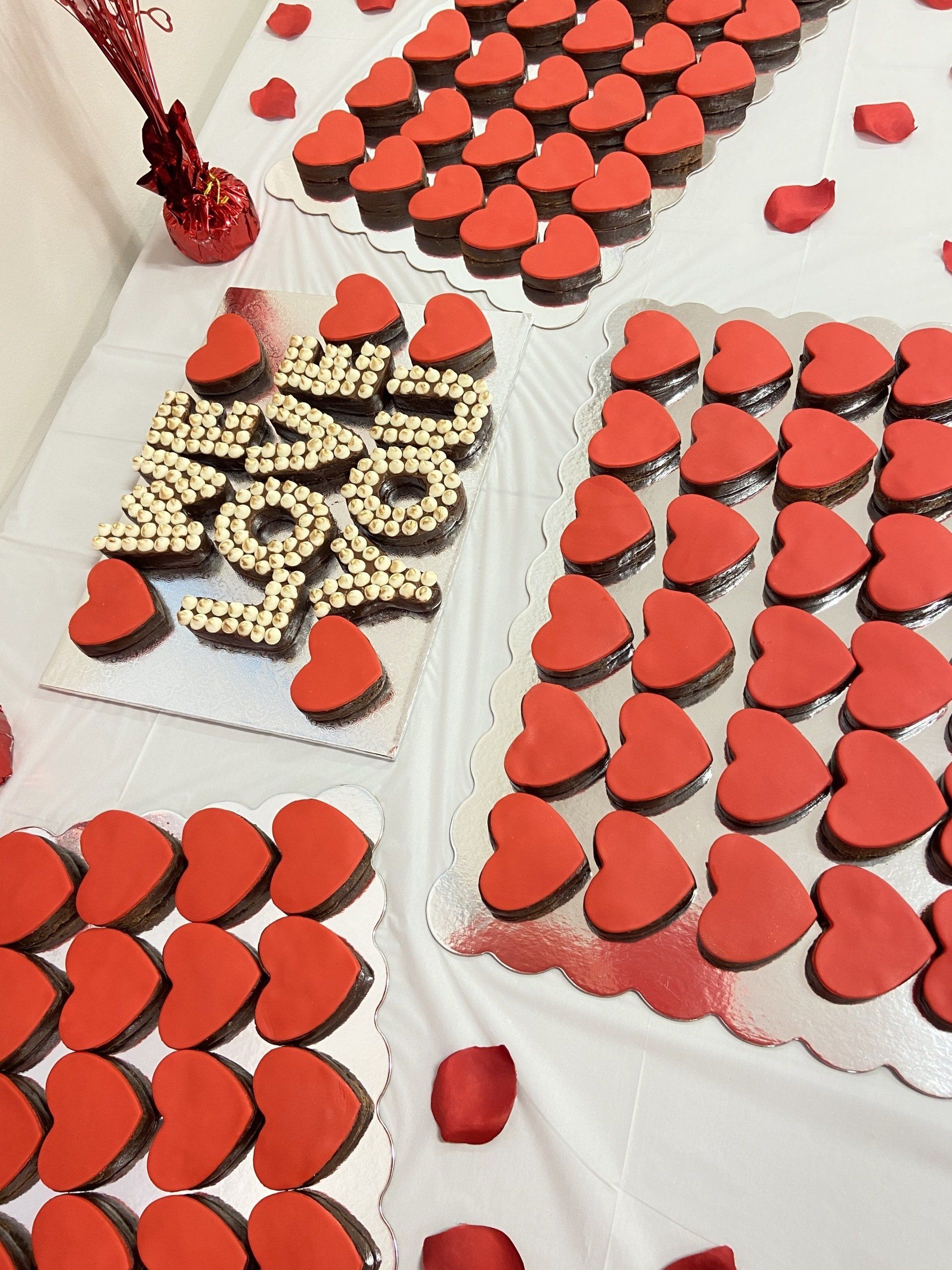 A table topped with red heart shaped cookies and rose petals