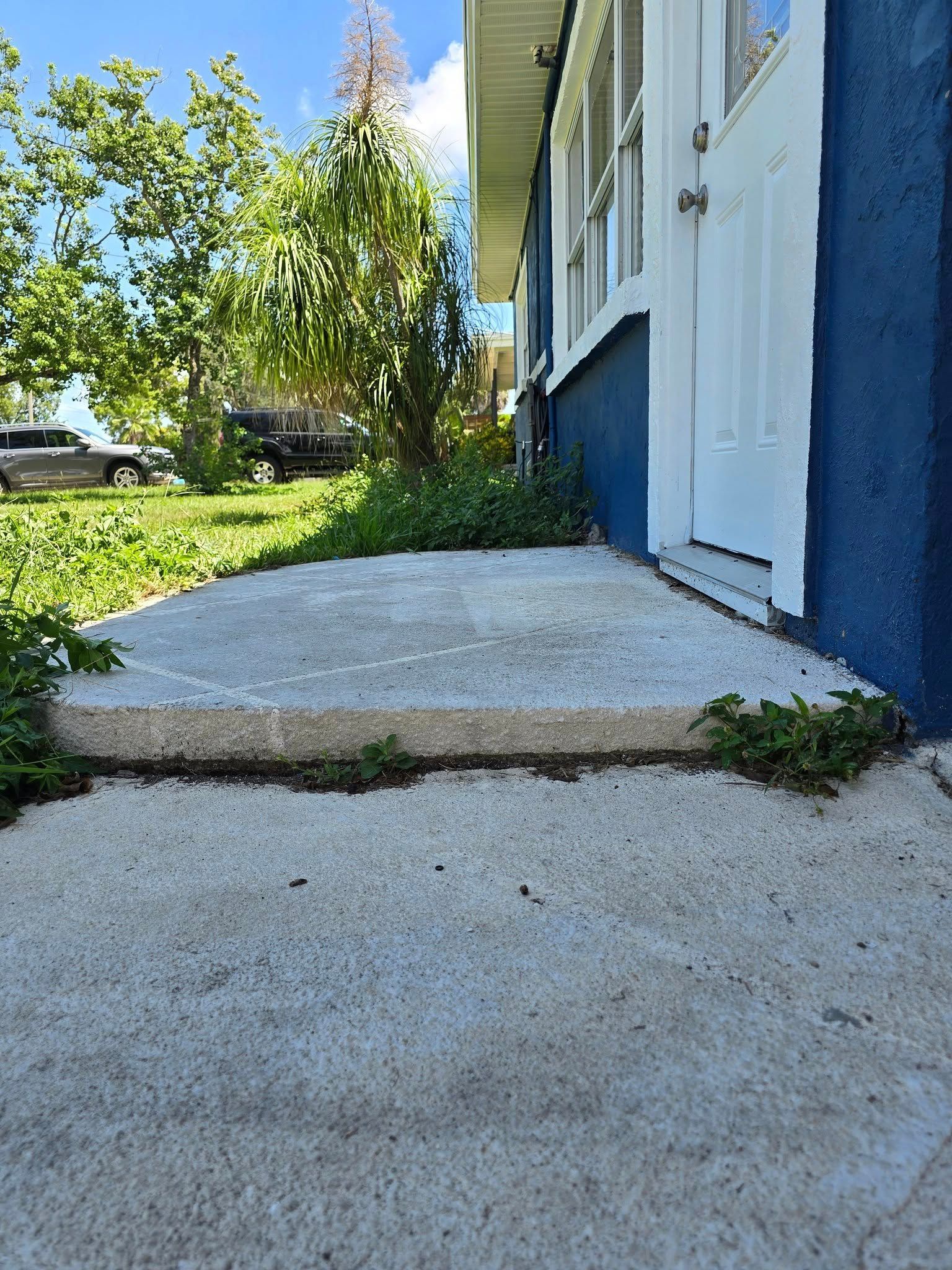 Cracked concrete steps leading to a blue house with white trim, viewed beside a sunny yard.