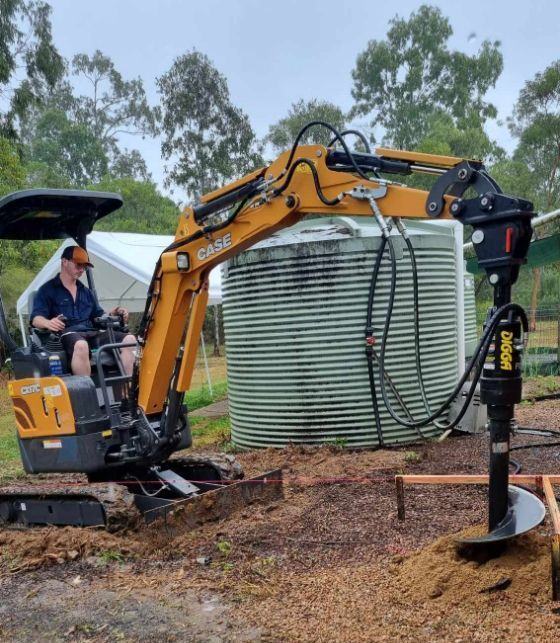 A Man Is Driving A Small Excavator In A Dirt Field — Blue Diesel & Equipment In Speewah, QLD