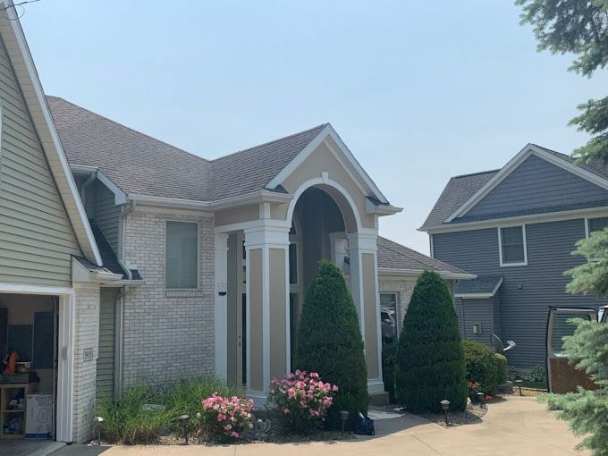 A house with a garage and a driveway is surrounded by trees and bushes.