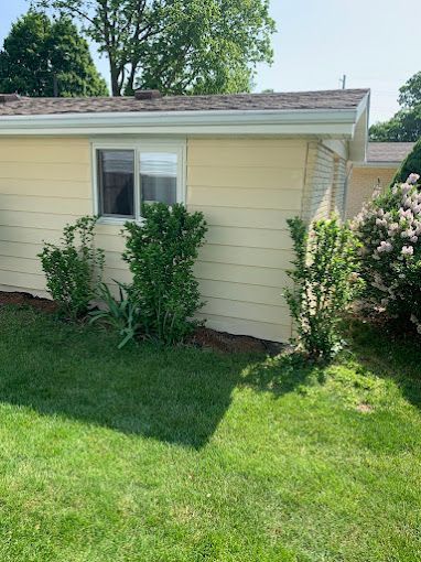 A yellow house with a window and a lush green lawn in front of it.
