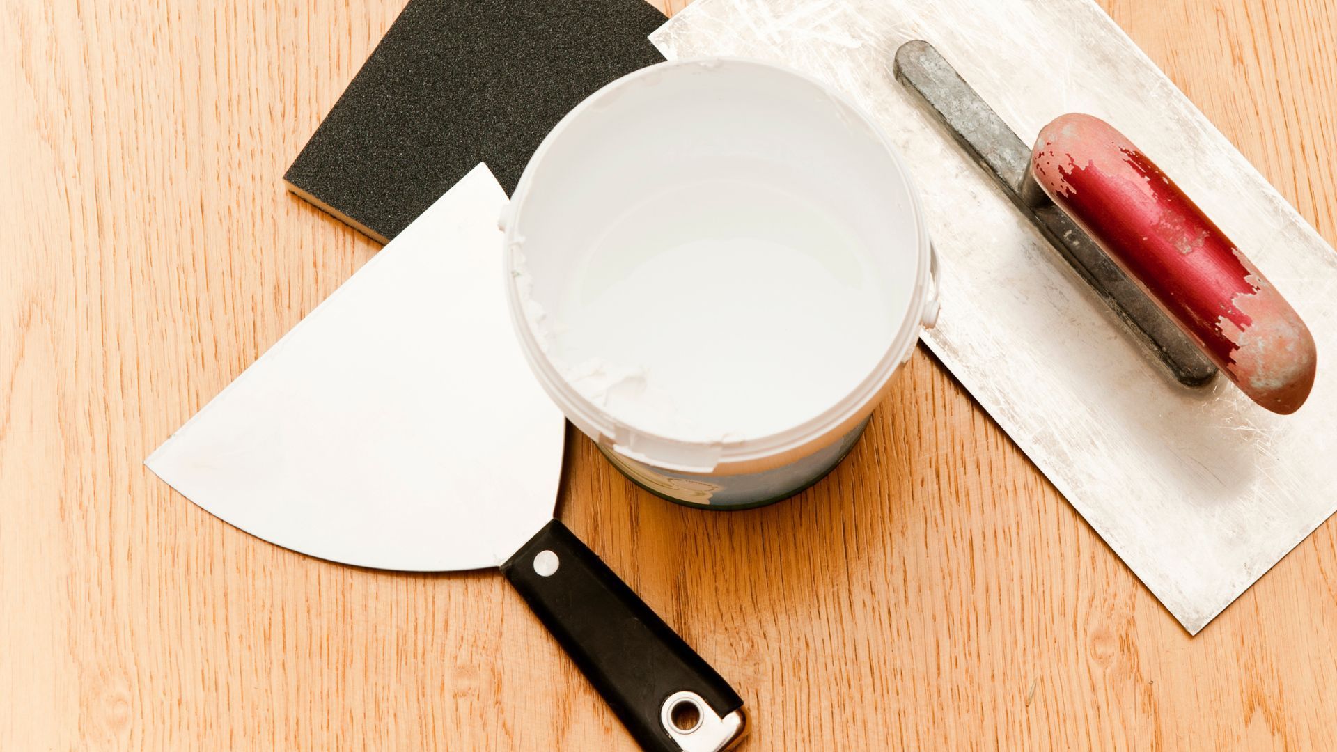 A spatula is sitting on a wooden table next to a bowl of plaster