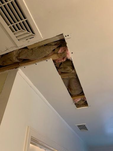 A hole in the ceiling of a room with insulation coming out of it.
