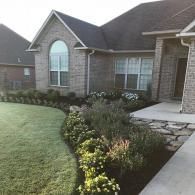 A brick house with a front garden featuring a stone walkway, green lawn, and manicured shrubs under an evening sky.