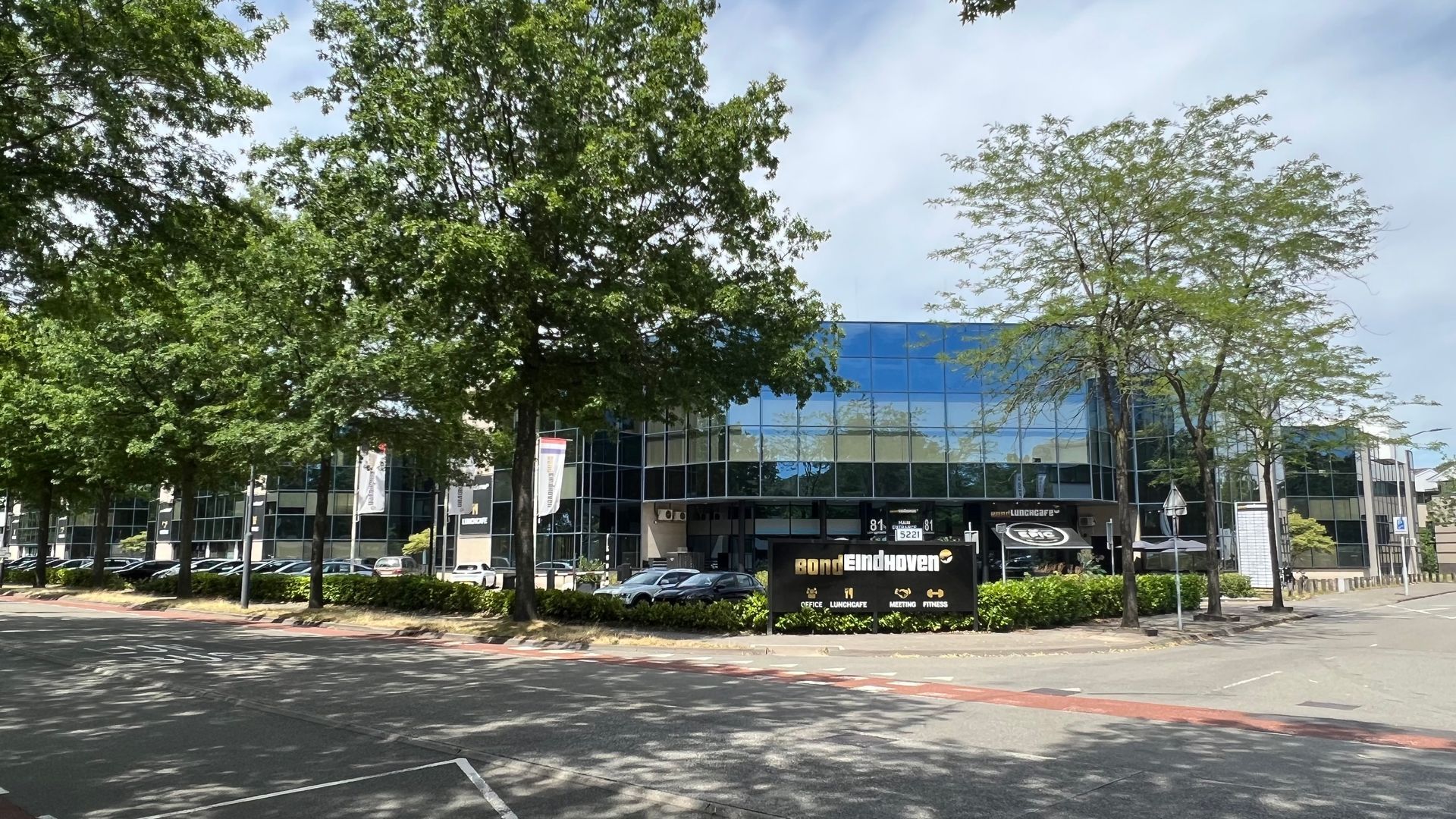 Kantoorgebouw met blauwe glazen gevel, omgeven door bomen en een rotonde.