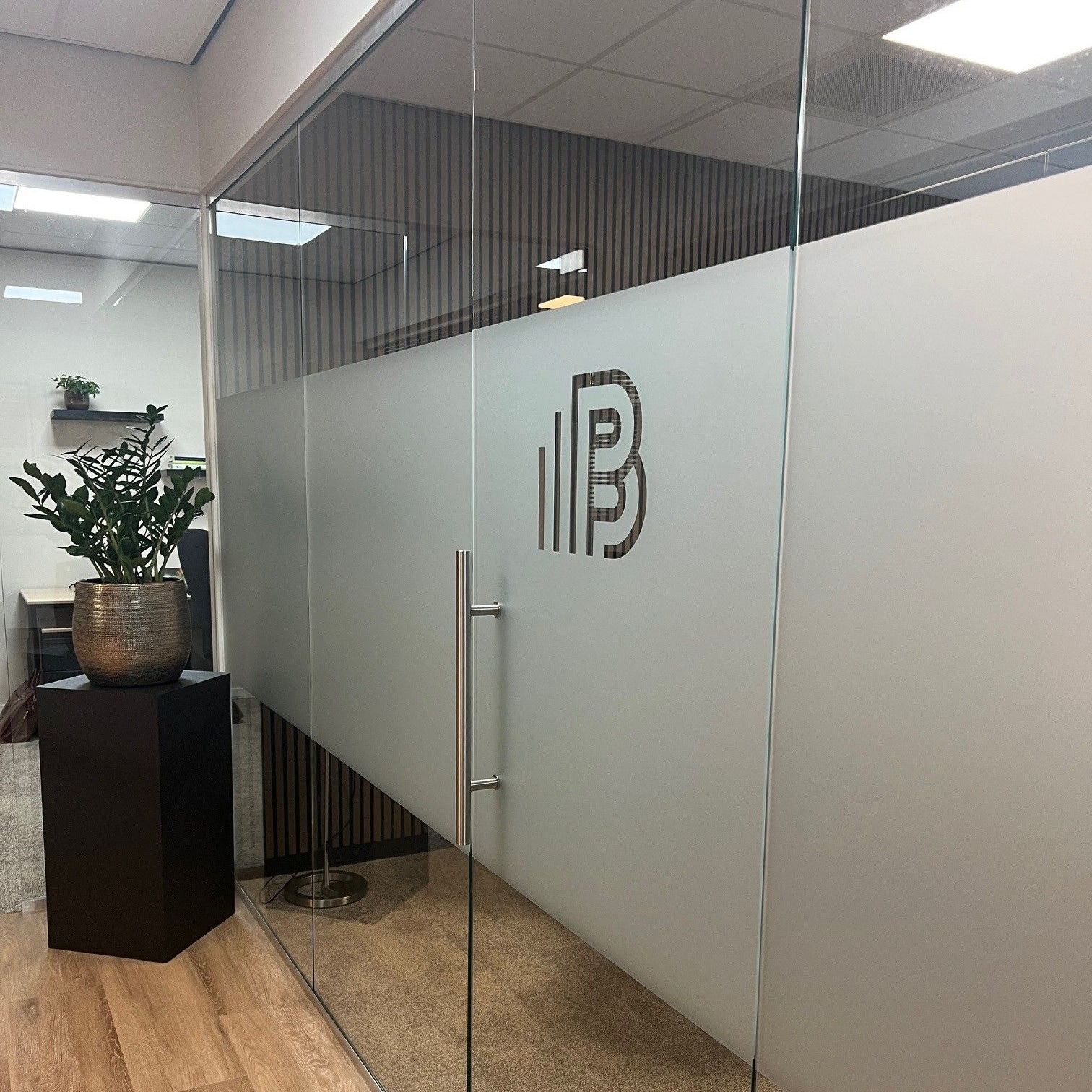 Glazen kantooringang met matglas, logo, plant en houten vloer.