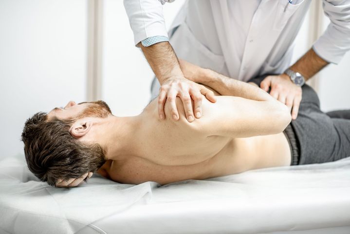 Doctor adjusting patient's back on a white examination table, wearing a white coat.