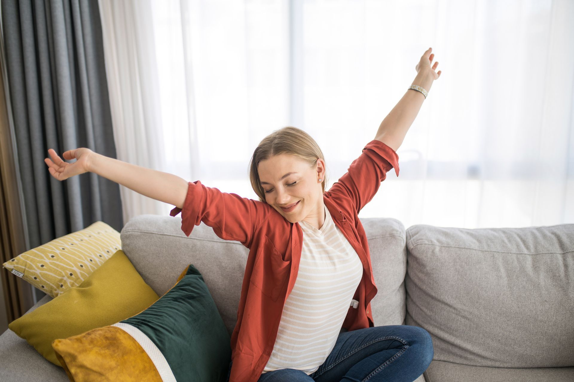 Woman sitting on a couch with arms raised, stretching and smiling. Woman sitting on a couch with arms raised, stretching and smiling.