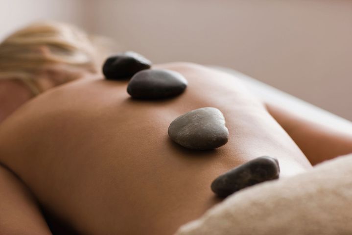 Person receiving hot stone massage on their back, stones placed along spine.