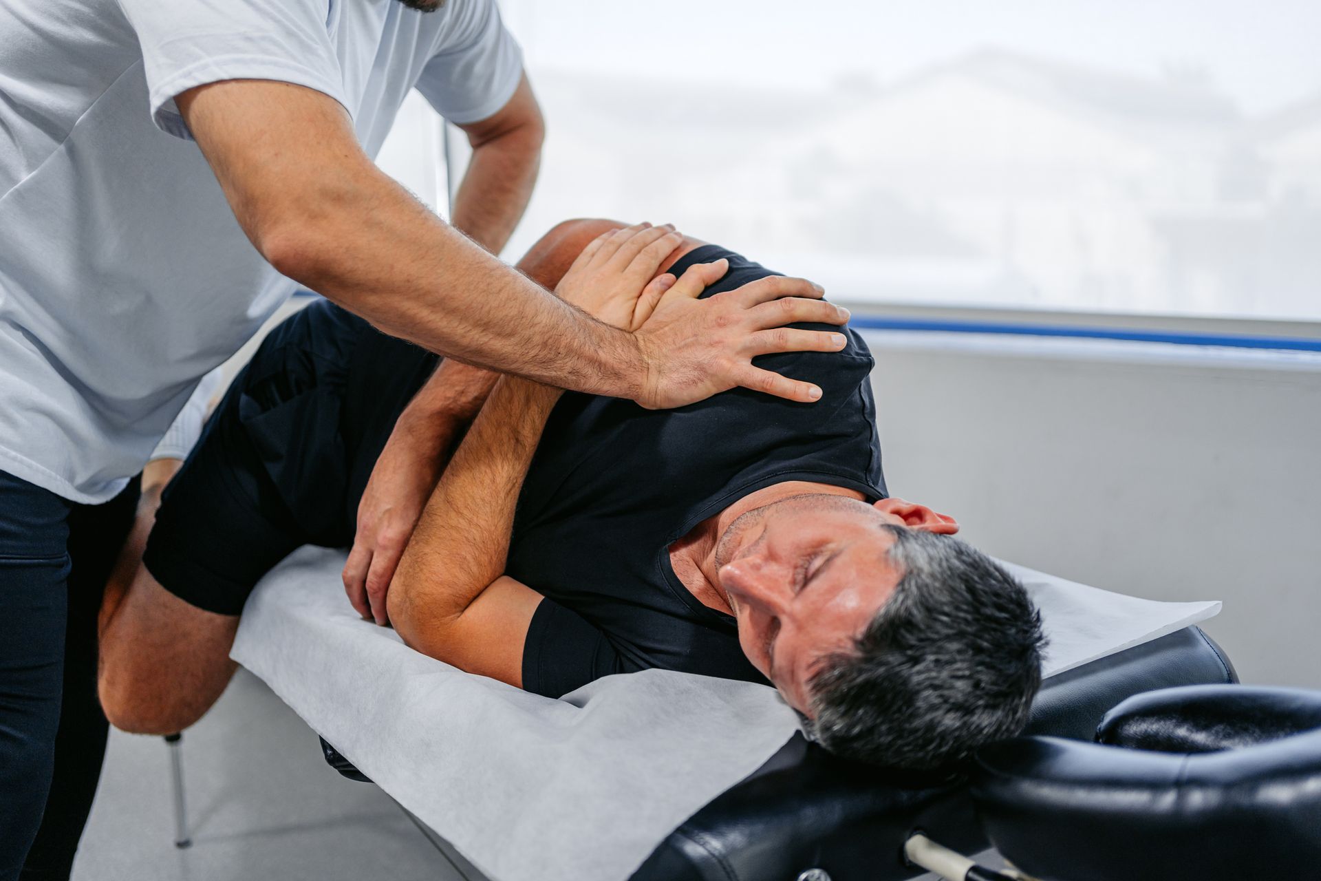 Man receiving chiropractic adjustment on a table. Practitioner holds his arm and shoulder.