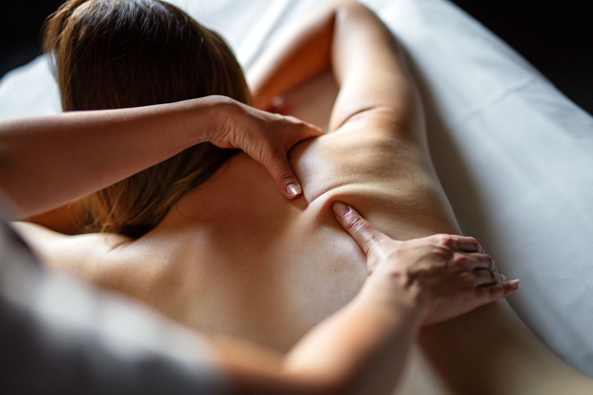 Hands giving a massage on a person's bare back and shoulder, indoors on a massage table.