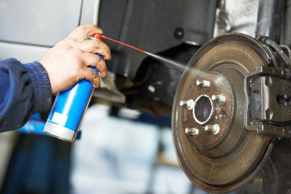 A Person is Cleaning a Brake Disc With a Spray Can — Sprint Mufflers, Exhausts & Mechanical Repairs in Stuart, NT
