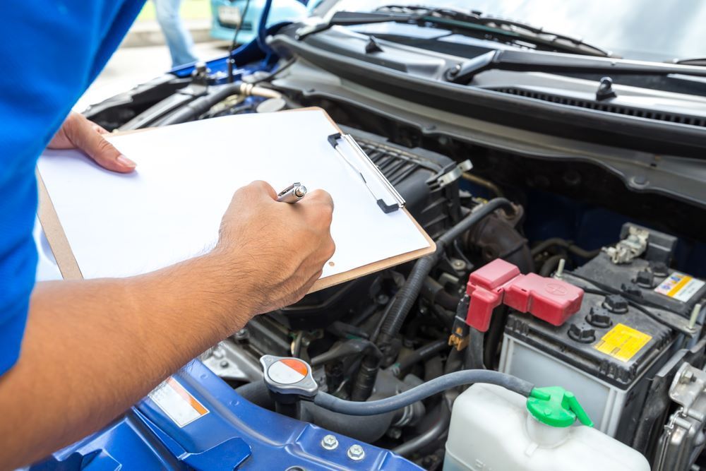 A Man is Writing on a Clipboard While Looking Under the Hood of a Car — Sprint Mufflers, Exhausts & Mechanical Repairs in Stuart, NT