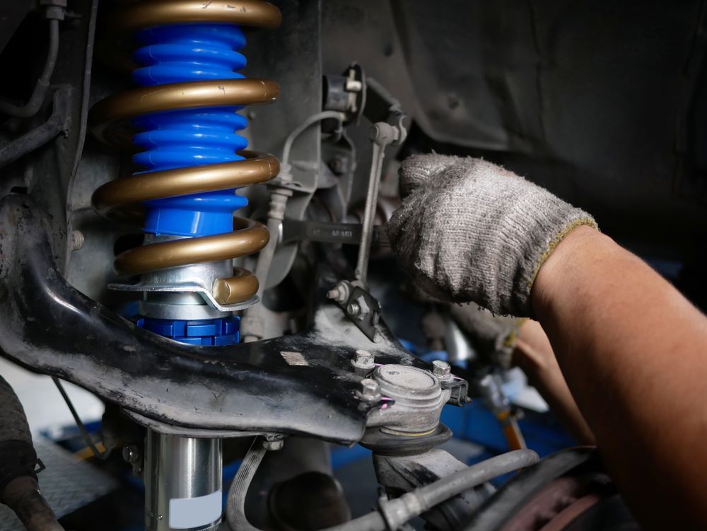 A Person is Working on a Shock Absorber on a Car — Sprint Mufflers, Exhausts & Mechanical Repairs in Stuart, NT