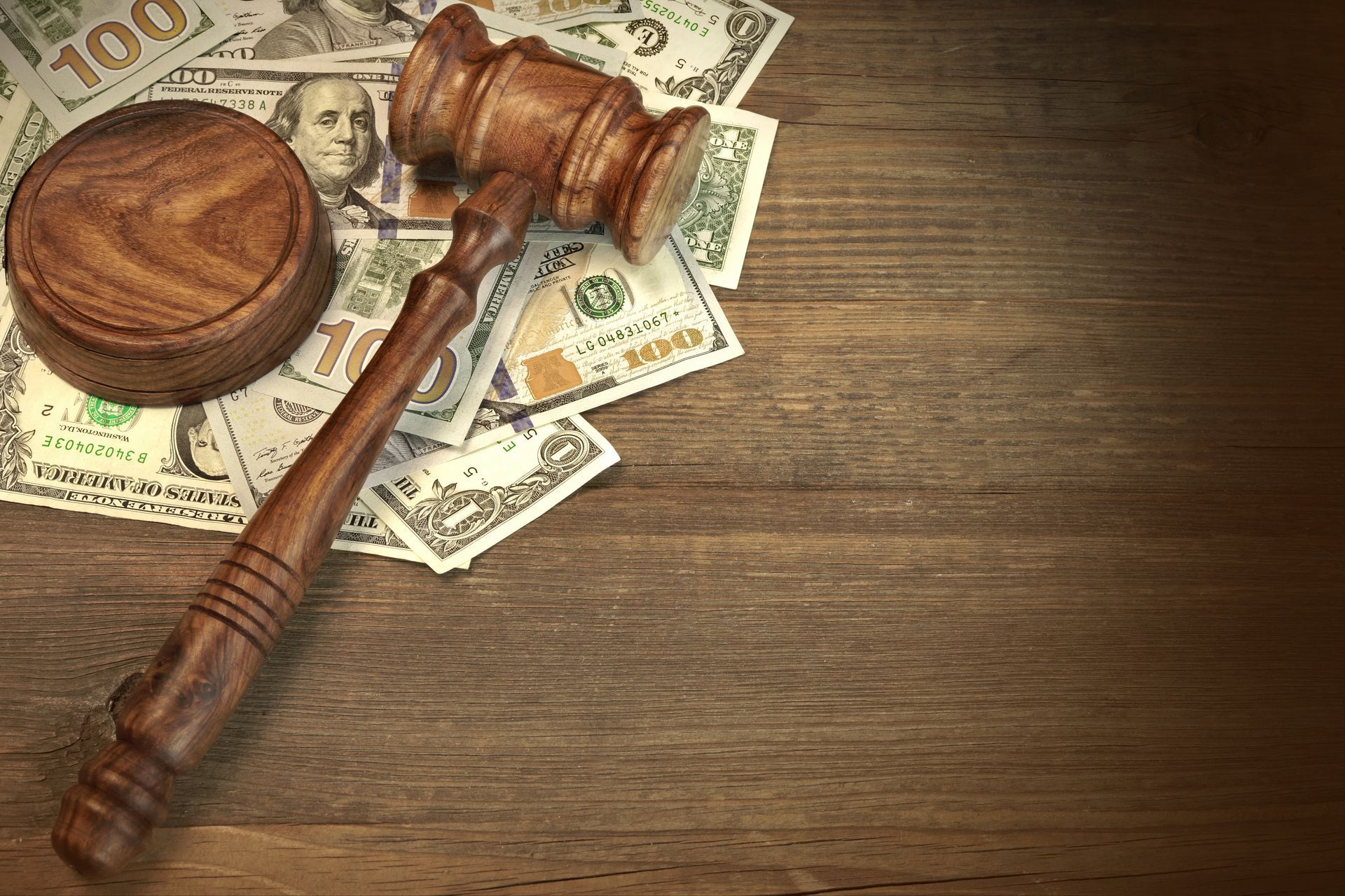 A wooden judge 's gavel is sitting on top of a pile of money on a wooden table.