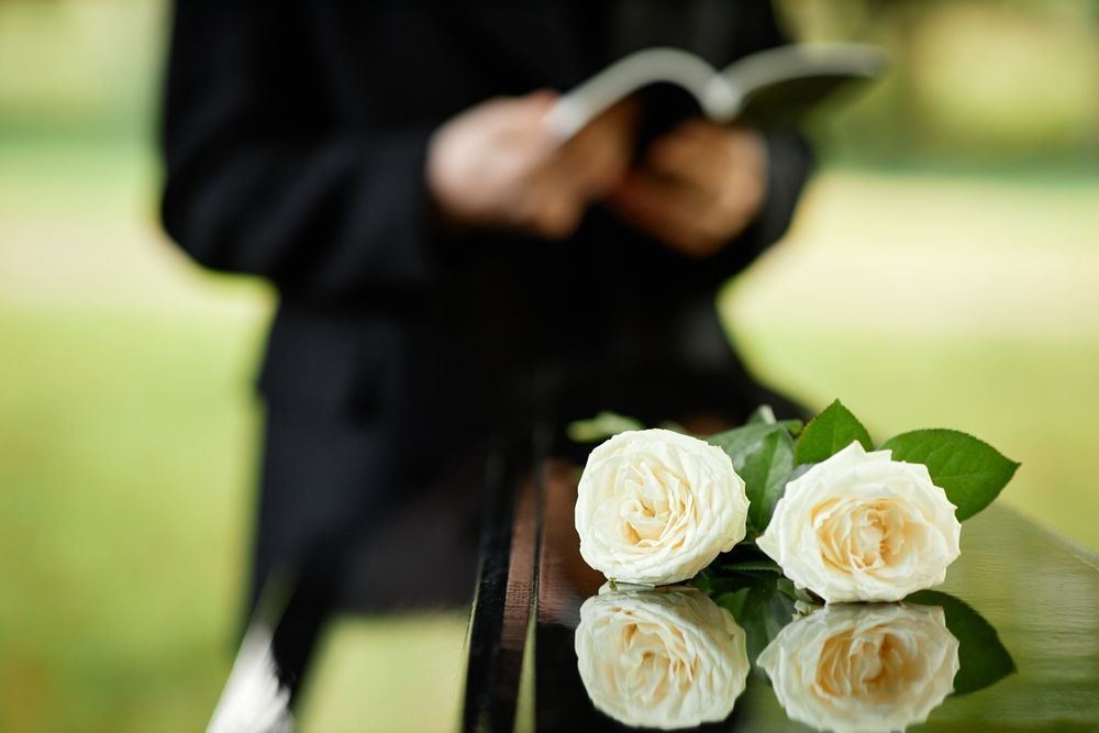 A Man Is Reading A Book Next To Two White Roses On A Table — Territory Funerals In Yarrawonga, NT