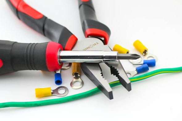 Close-up of electrician's tools: screwdriver, pliers, wire connectors, and green wire on a white surface.