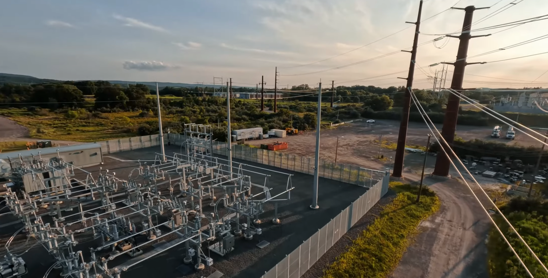 An aerial view of a power substation with electrical equipment, lines, and pylons.