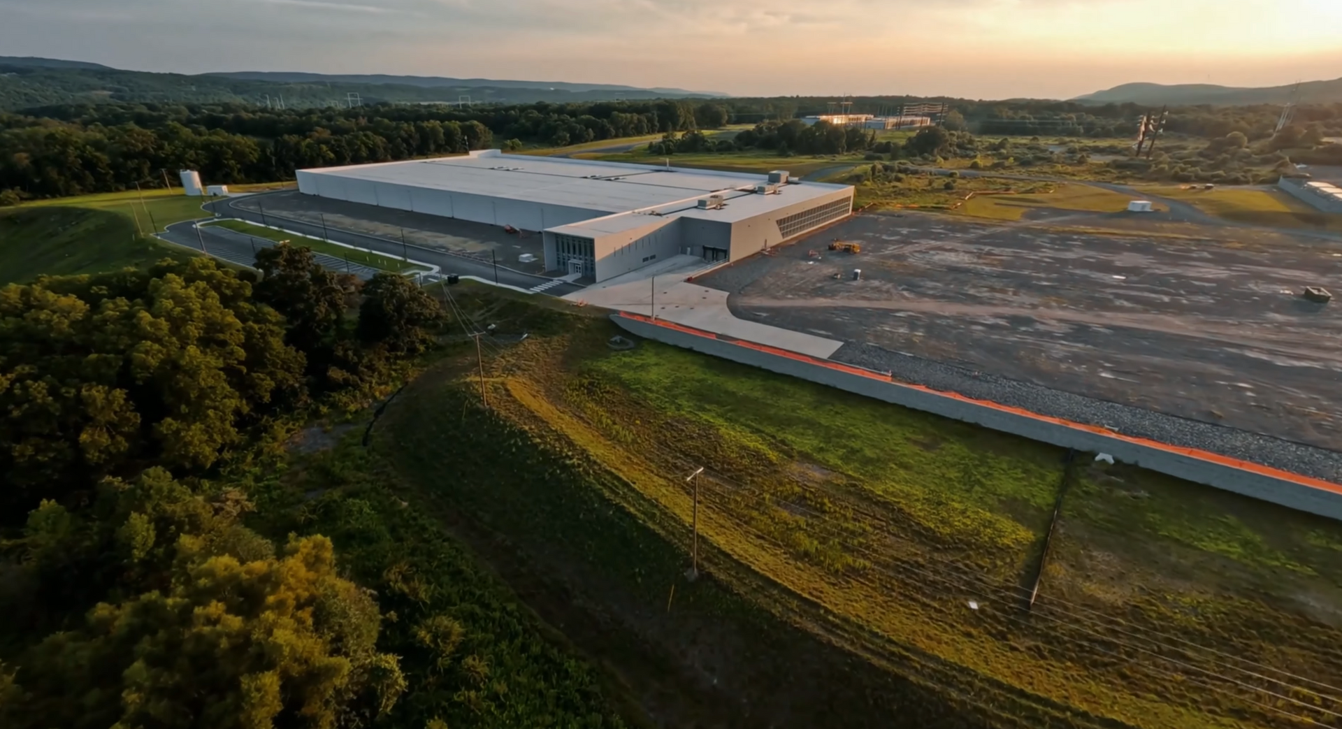 Aerial view of a nuclear power plant with two cooling towers releasing steam. Lush green forest surrounds the facility.