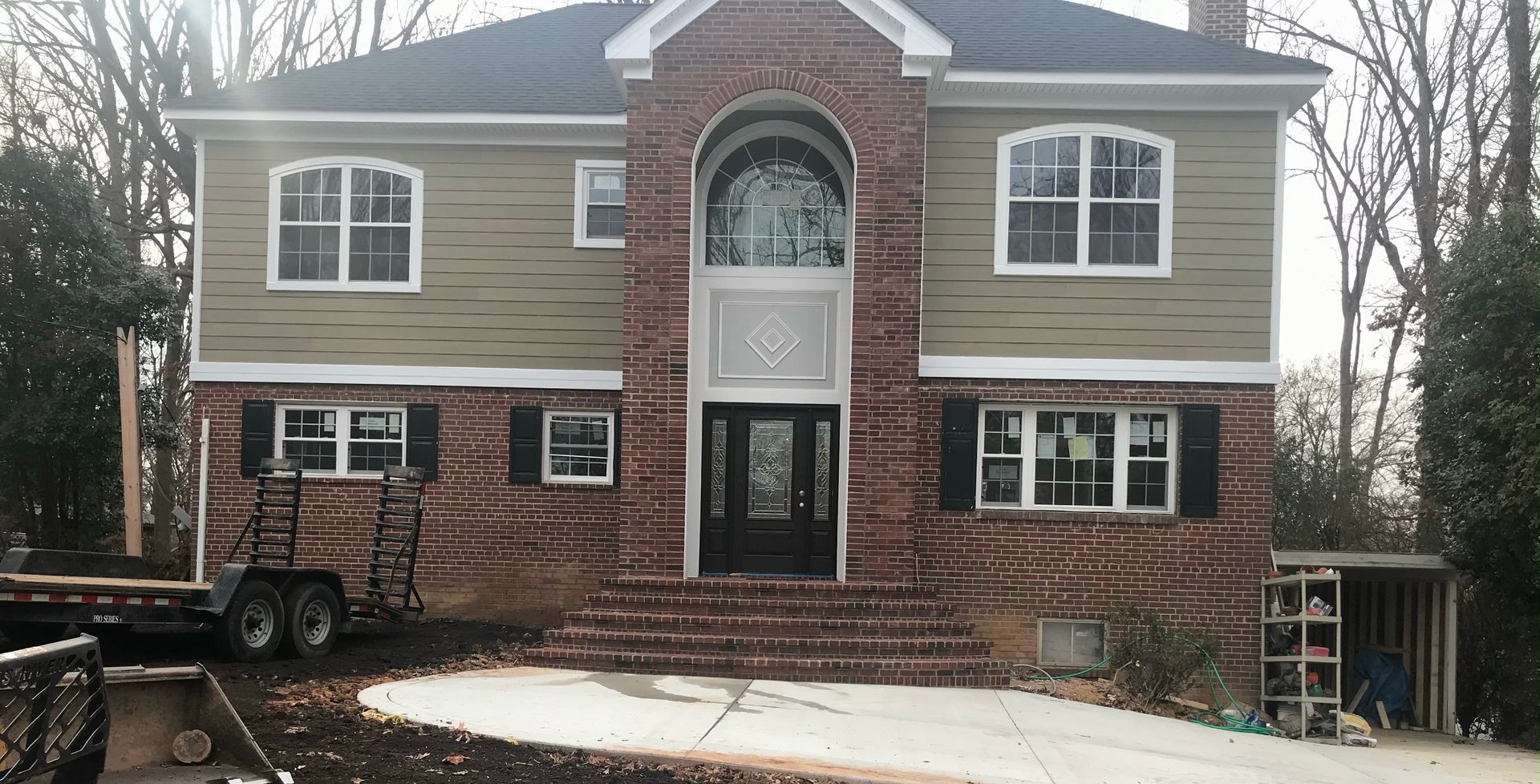 Two-story house with brick and siding, arched entryway, and front steps. A trailer sits in the yard.