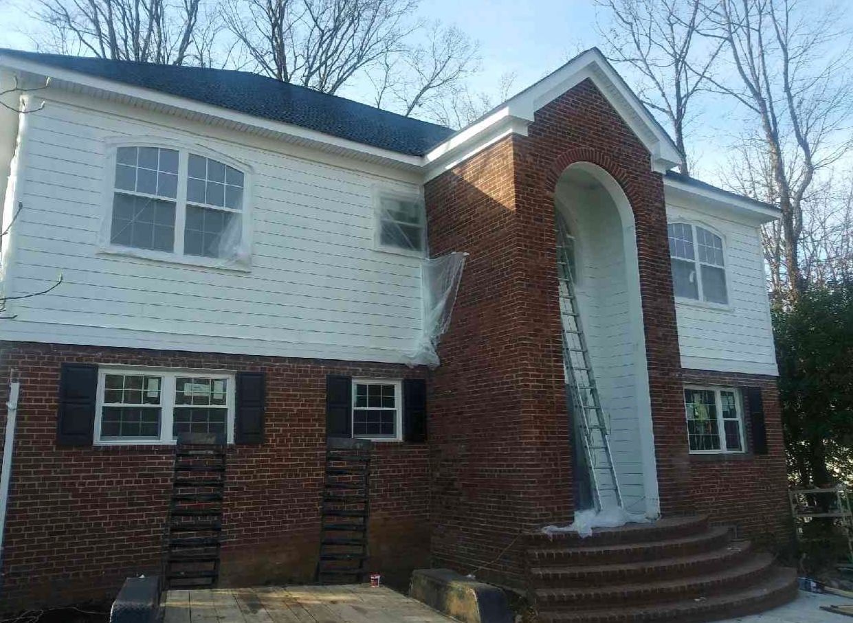 Two-story house undergoing renovation; brick facade, white siding, arched entrance, ladder present.