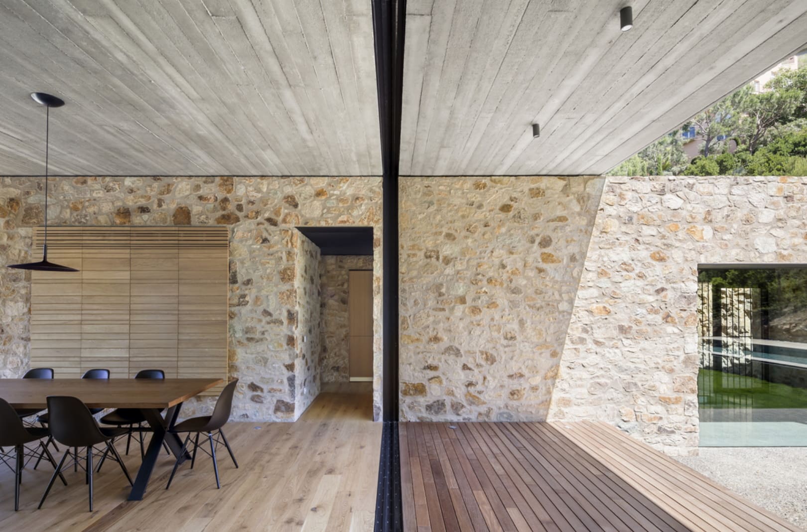The dining room with a stone wall, opens to the outside, featuring a minimalist window frame and modern design