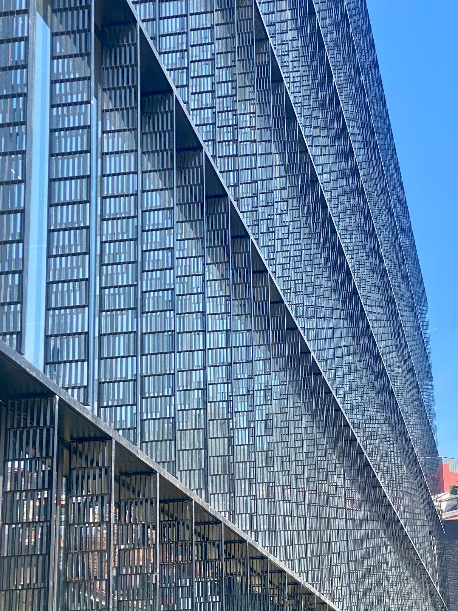 A detailed view of the façade of a contemporary building showcasing OTIIMA's minimalist window framing. The large glass panels reflect the surrounding architecture, emphasizing the seamless integration and elegance of OTIIMA's design in modern construction