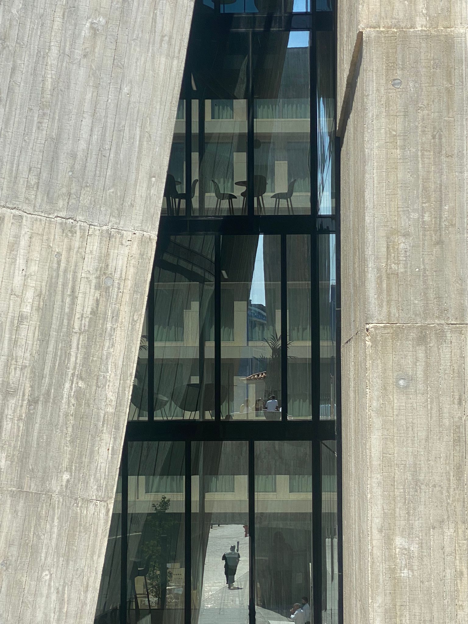 A detailed view of a contemporary building showcasing OTIIMA's minimalist window framing. The large glass panels reflect the surrounding architecture, emphasizing the seamless integration and elegance of OTIIMA's design in modern construction