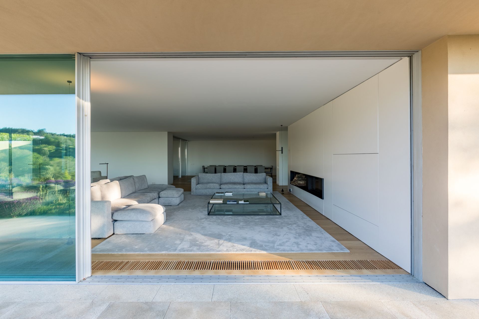 Modern living room with large sliding glass windows by OTIIMA, showcasing seamless indoor-outdoor transition.