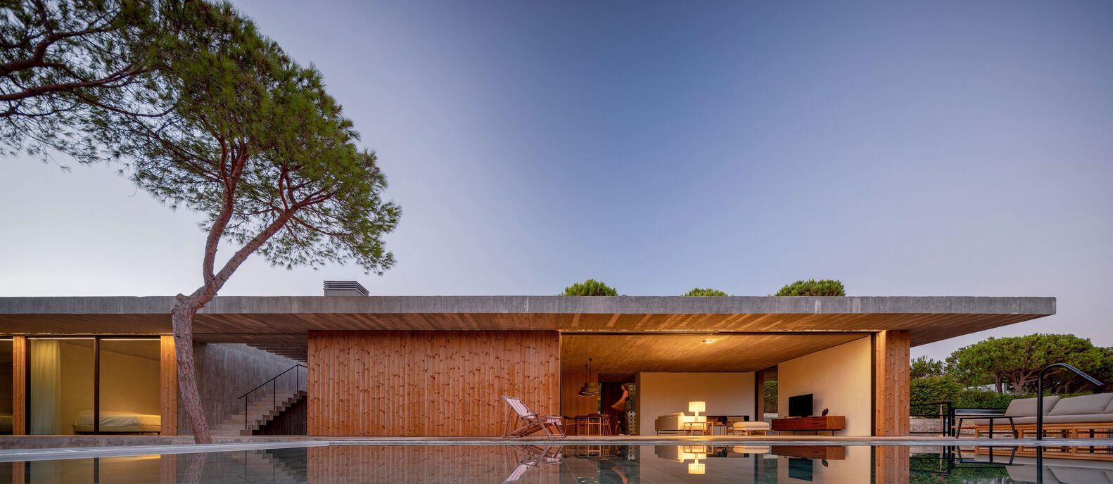 Contemporary wooden house with outdoor leisure area and pool, showcasing minimalist windows by OTIIMA that blend seamlessly with the natural surroundings.