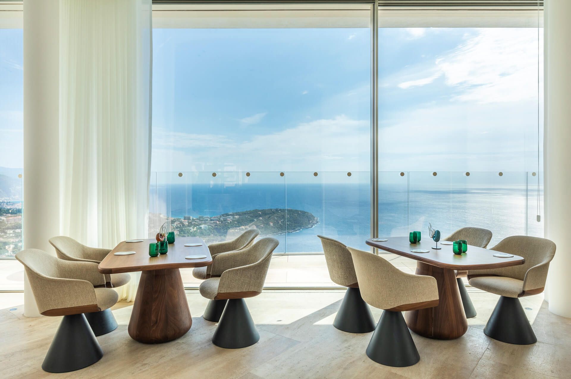 Sleek cliffside hotel with expansive glass windows offering panoramic views of the Riviera coastline.