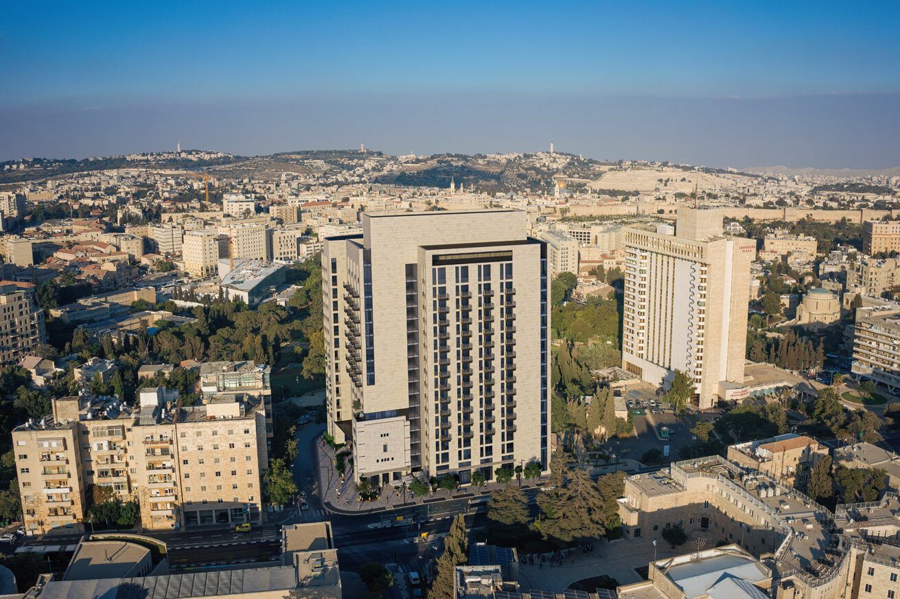 Panoramic view of Jerusalem cityscape seen through floor-to-ceiling windows in a modern hotel room.