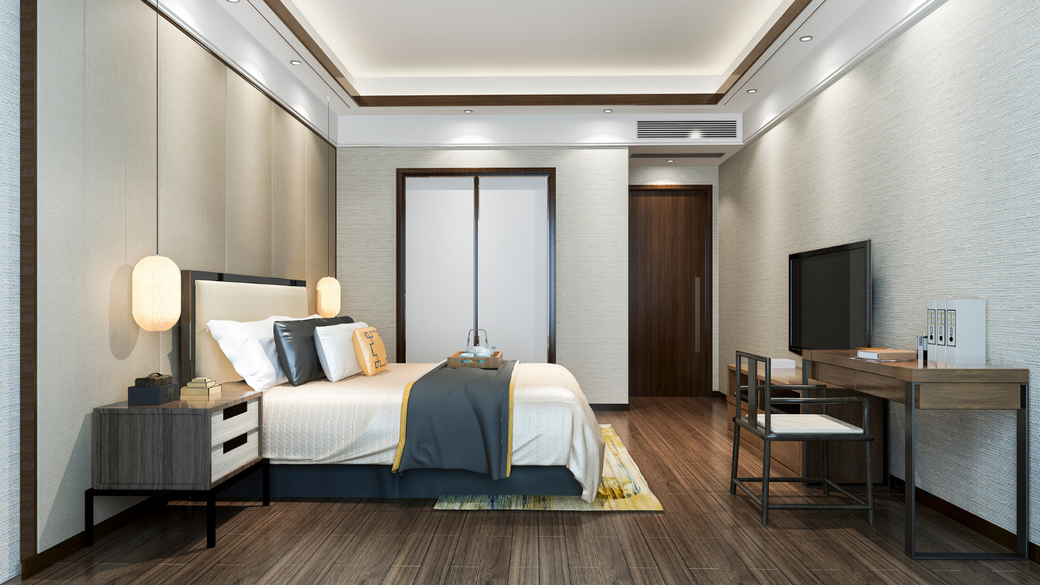Modern hotel bedroom with a neatly made bed, bedside lamps, desk, TV, and warm wood floors.