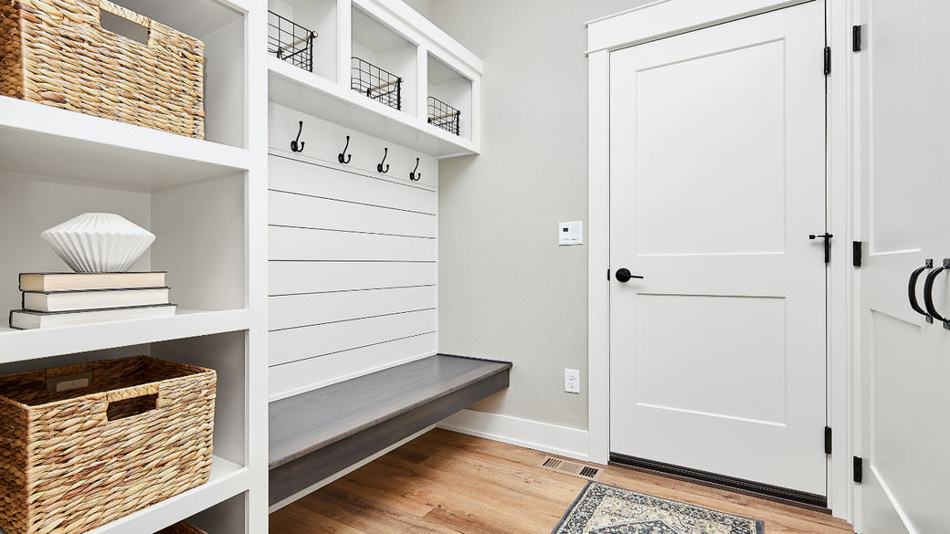Bright entryway with white built-in storage, bench, hooks, gray walls, and hardwood floor