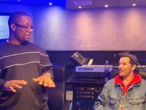 Two people talking in a studio, with audio equipment and blue lighting in the background