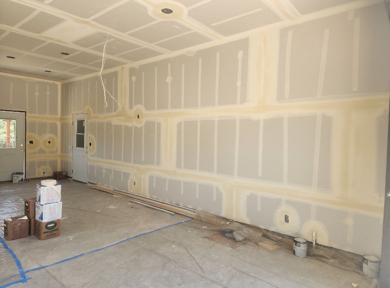 Interior of a room under construction, with drywall installed, mudded seams, and unfinished ceiling.