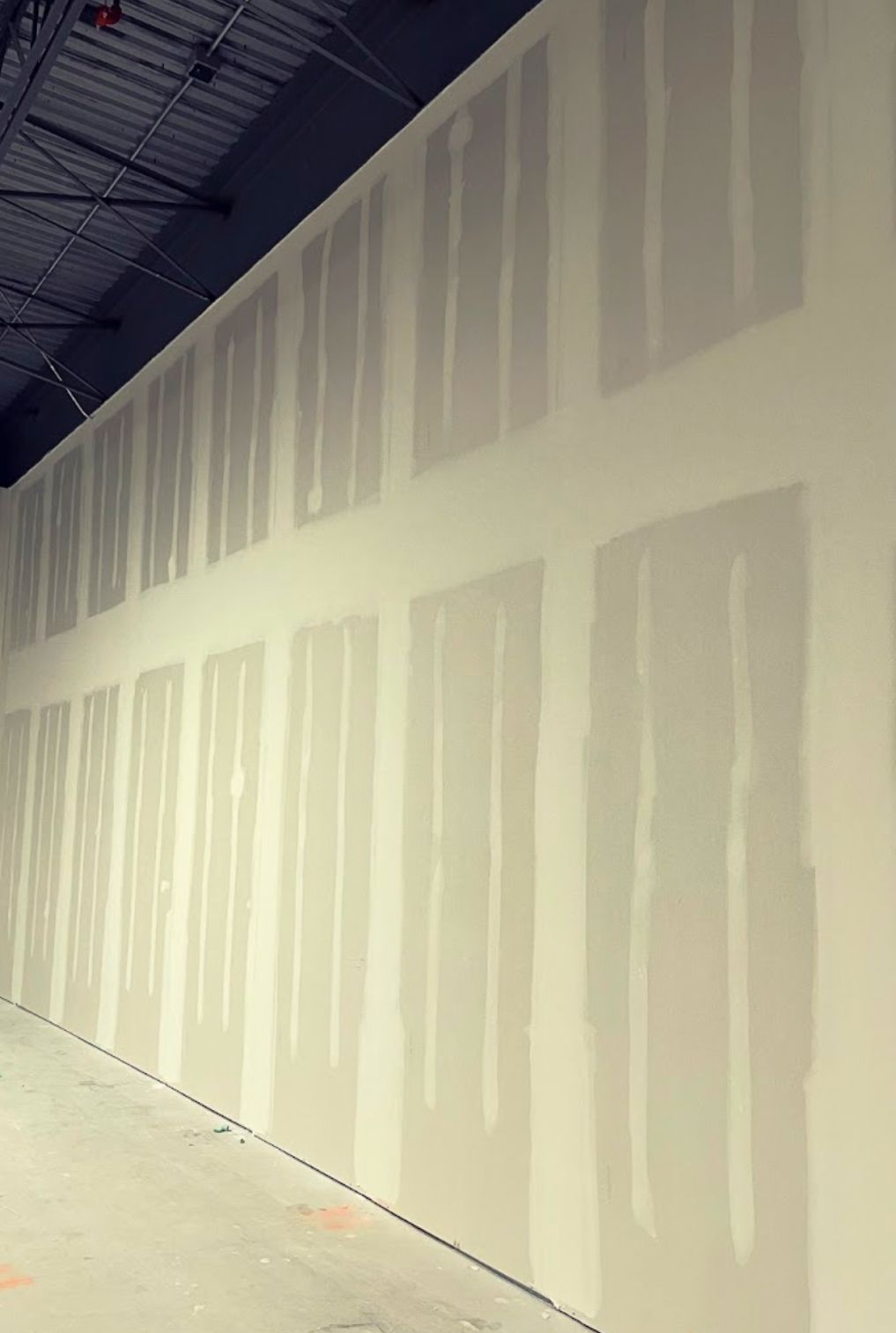 A long, drywall-covered interior wall in a commercial space, likely under construction.